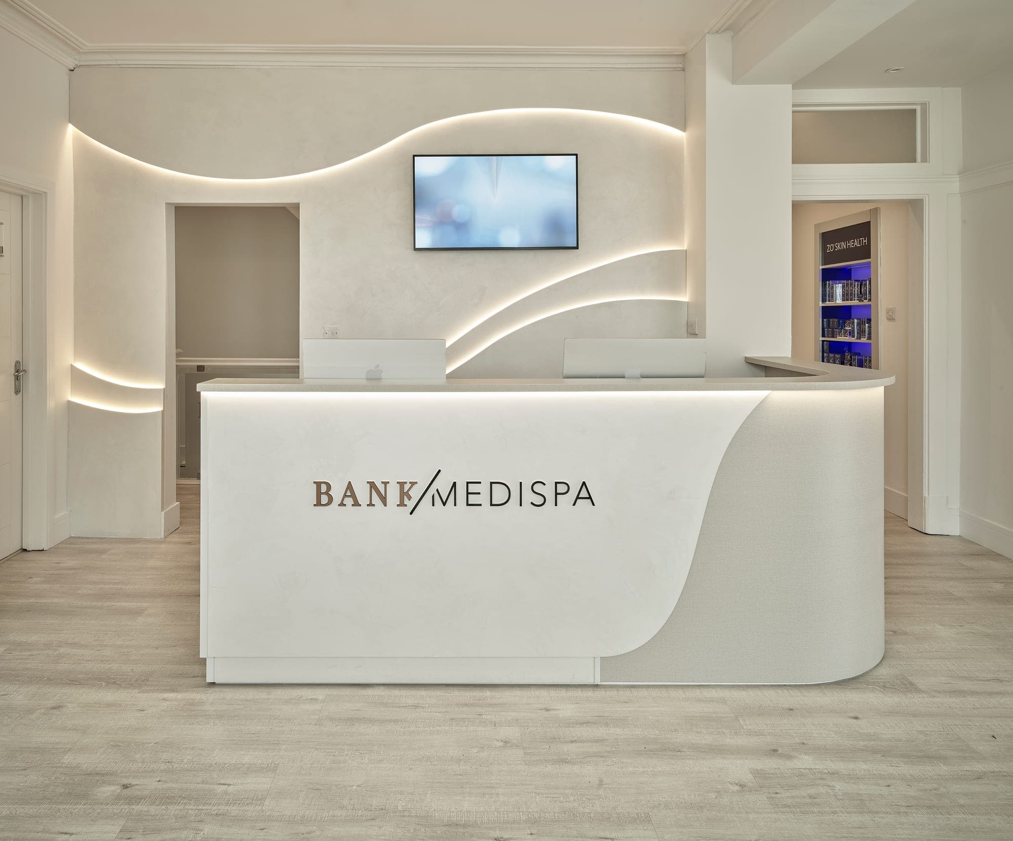 Curved white reception desk and backlit feature wall at Bank Medi Spa, Hale