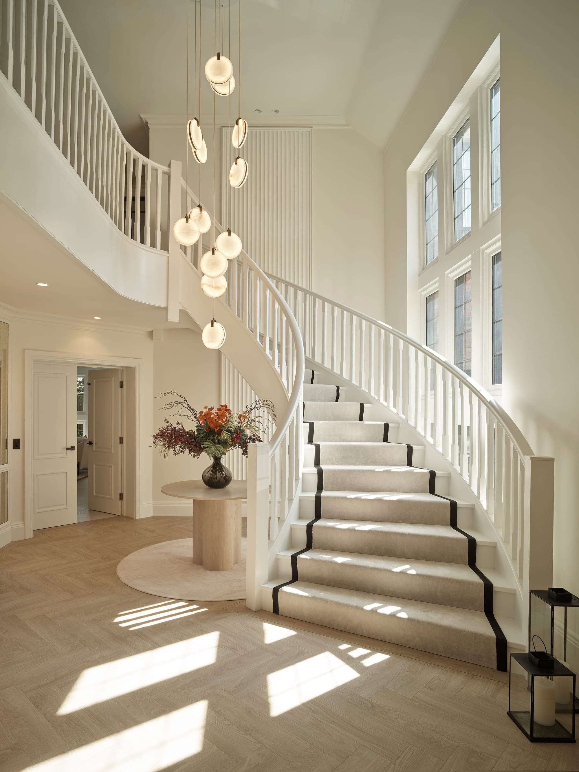 Curved staircase with a black-edged runner and cluster pendant in the entrance hall of a Prestbury family home, Cheshire